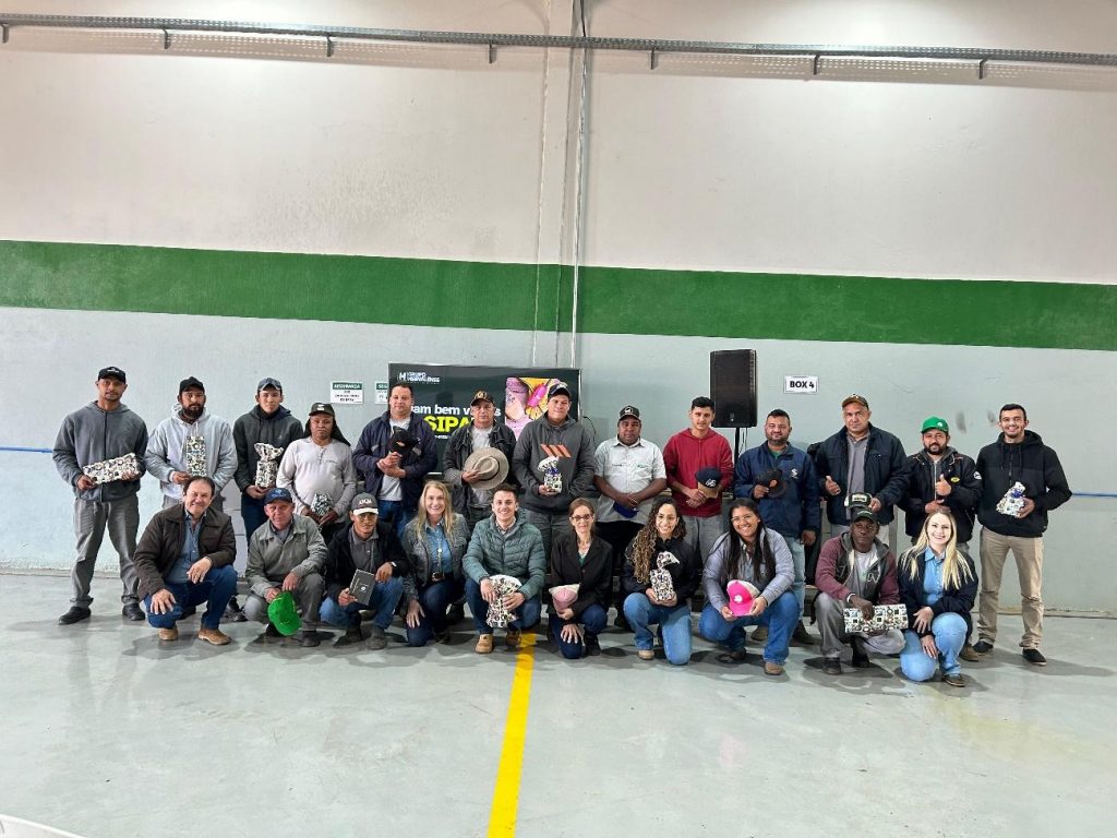 Um grupo de colaboradores, incluindo homens e mulheres, posando juntos dentro de um galpão industrial. Todos estão sorrindo, usando camisetas e uniformes da empresa, com alguns segurando brindes, mostrando o sucesso da 6ª SIPATR.