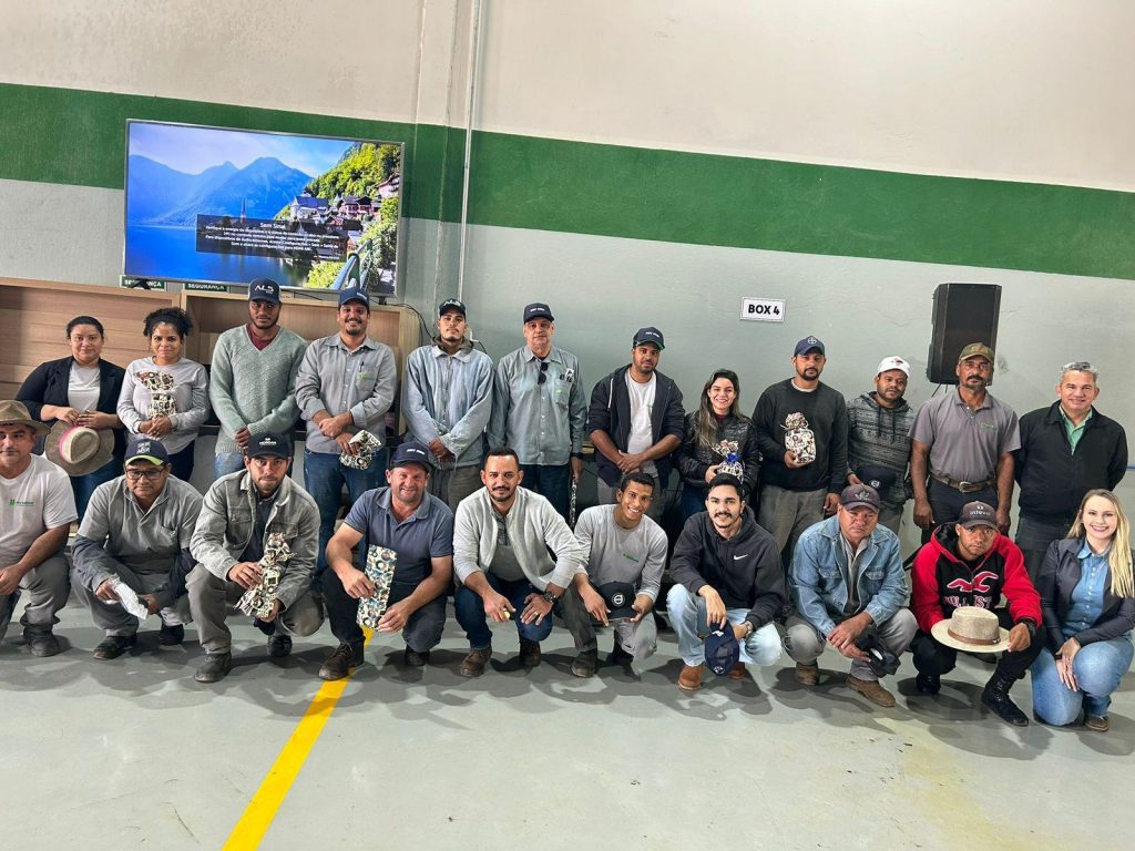 Um grupo de colaboradores, incluindo homens e mulheres, está alinhado e posando para uma foto em um galpão. Todos estão sorrindo e segurando brindes que receberam durante a 6ª SIPATR.