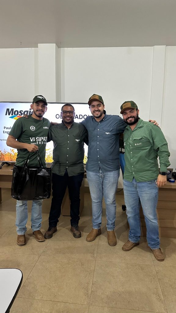 Quatro participantes da 4ª Semana Técnica do Grupo Hervalense posam para foto ao lado de telão da Mosaic Fertilizantes.