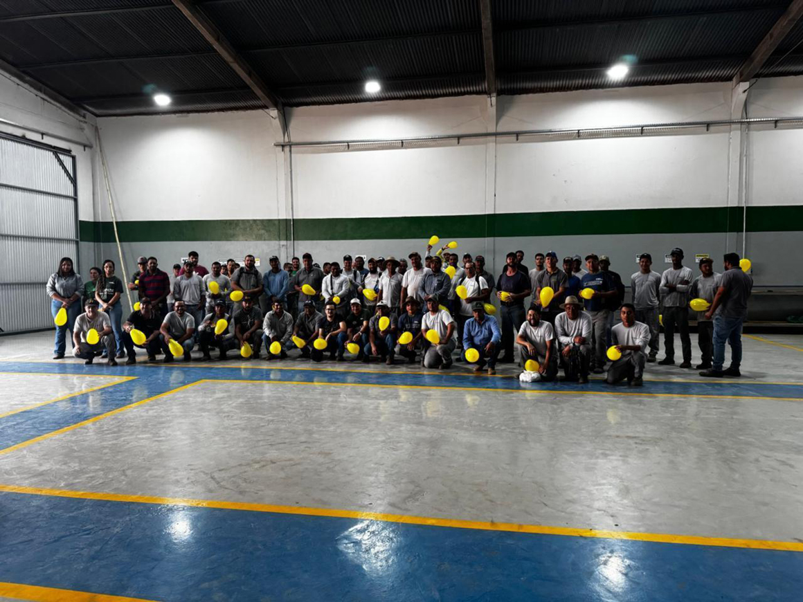 Um grande grupo de colaboradores do Grupo Hervalense posando em um galpão amplo, com balões amarelos em mãos, como parte das atividades do Setembro Amarelo. O ambiente é amplo e industrial, reforçando a integração da campanha no cotidiano da empresa.