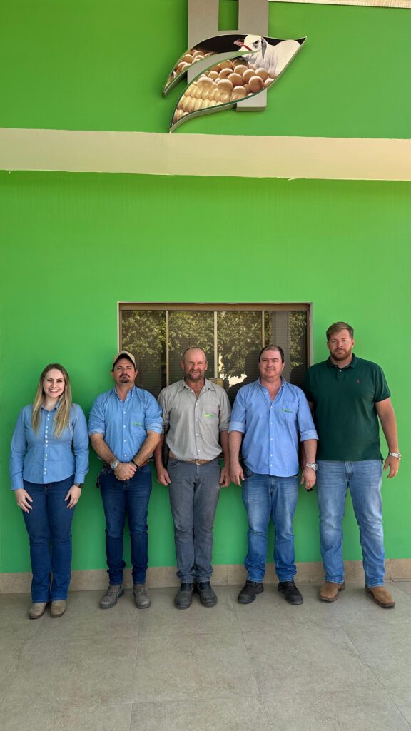 Foto em grupo de cinco profissionais do Grupo Hervalense, posando lado a lado em frente a um prédio com fachada verde e logotipo em destaque na parte superior. Todos estão vestidos com camisas sociais em tons de azul, cinza e verde, representando a equipe técnica da empresa. A imagem transmite união, profissionalismo e valorização da agronomia no contexto do Dia do Agrônomo.