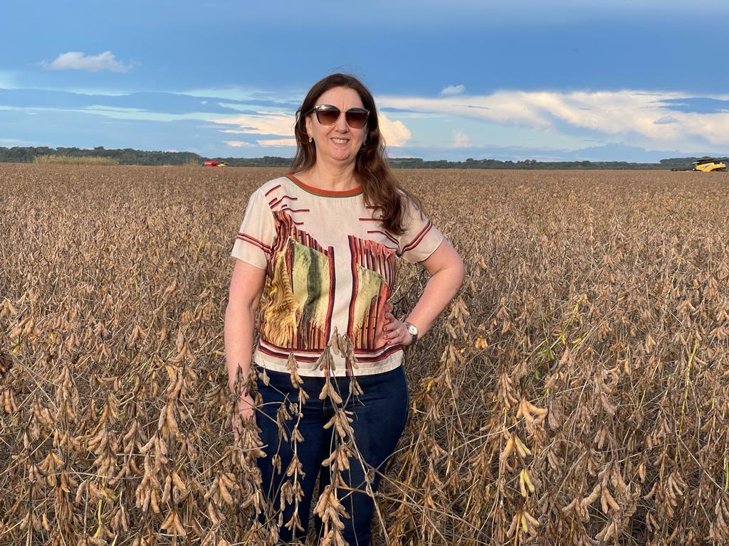 Maristela Cristofolli, diretora-administrativa da Hervalense, posa sorridente em meio a uma lavoura madura de soja sob céu azul com nuvens claras. Ela usa óculos escuros, blusa estampada em tons terrosos e calça jeans, transmitindo naturalidade e conexão com o campo — cenário que simboliza suas origens e o vínculo entre gestão e terra que marcam sua trajetória na empresa.