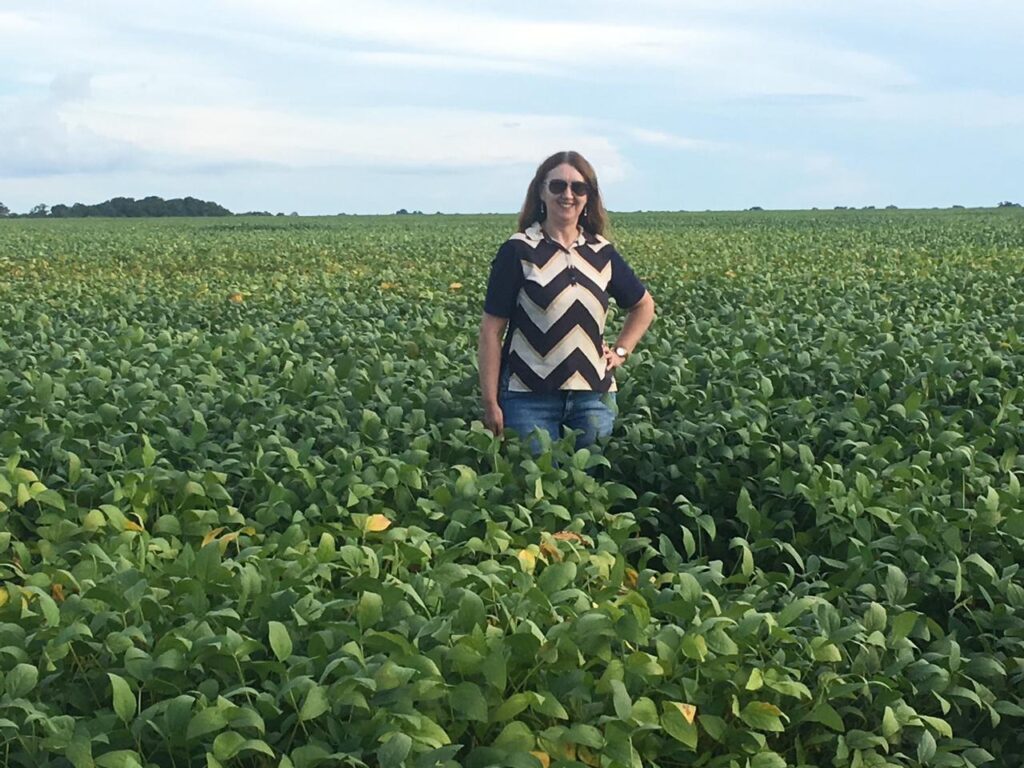 Maristela Cristofolli, diretora-administrativa da Hervalense, posa sorridente em meio a uma lavoura madura de soja sob céu azul com nuvens claras,